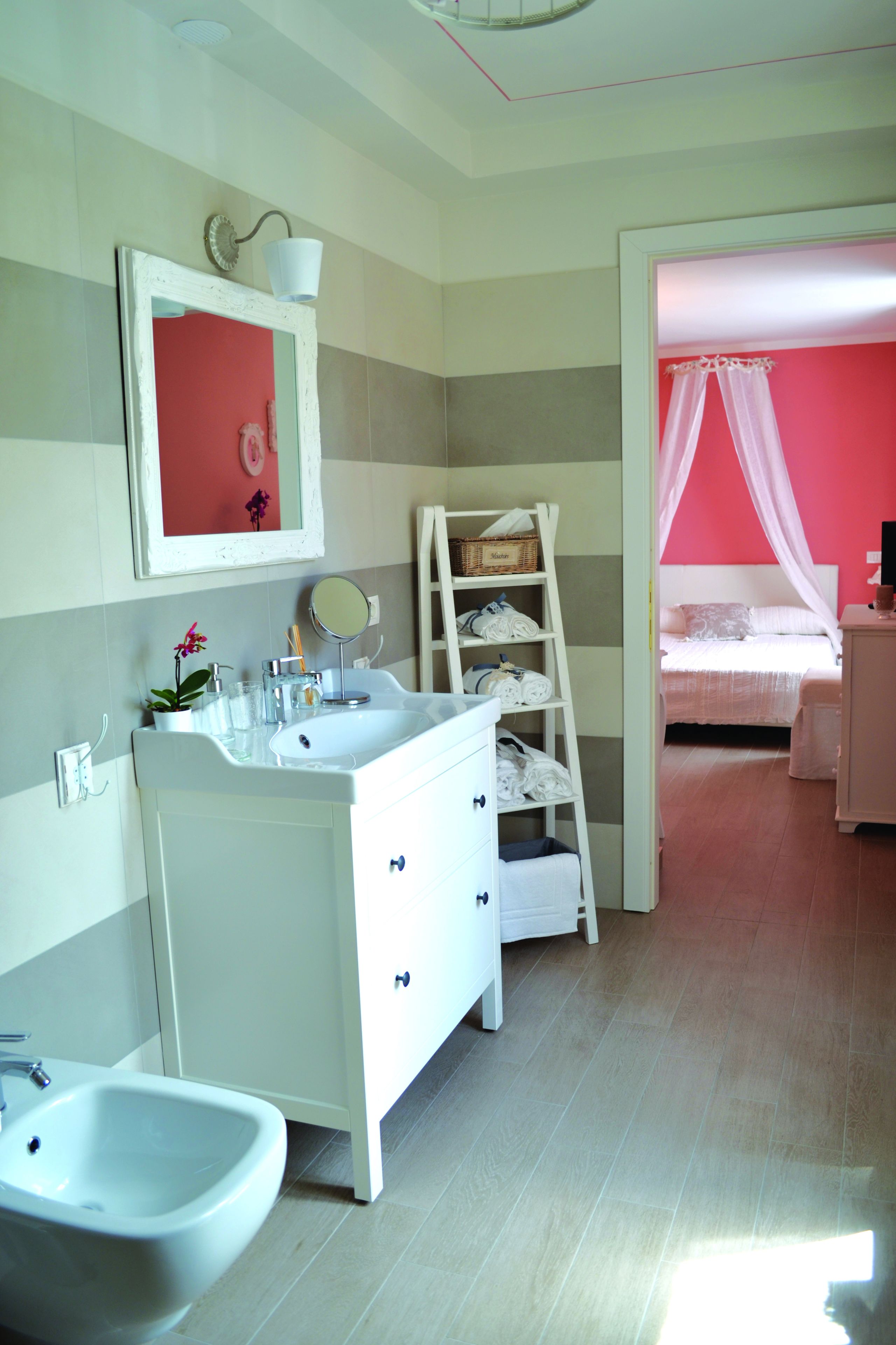 Een badkamer met een witte wasbak, spiegel en een witte wastafel. Er staat een ladder met handdoeken en een mand erop.