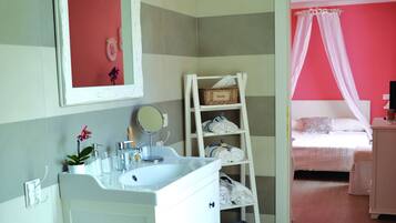 Een badkamer met een witte wasbak, spiegel en een witte wastafel. Er staat een ladder met handdoeken en een mand erop.