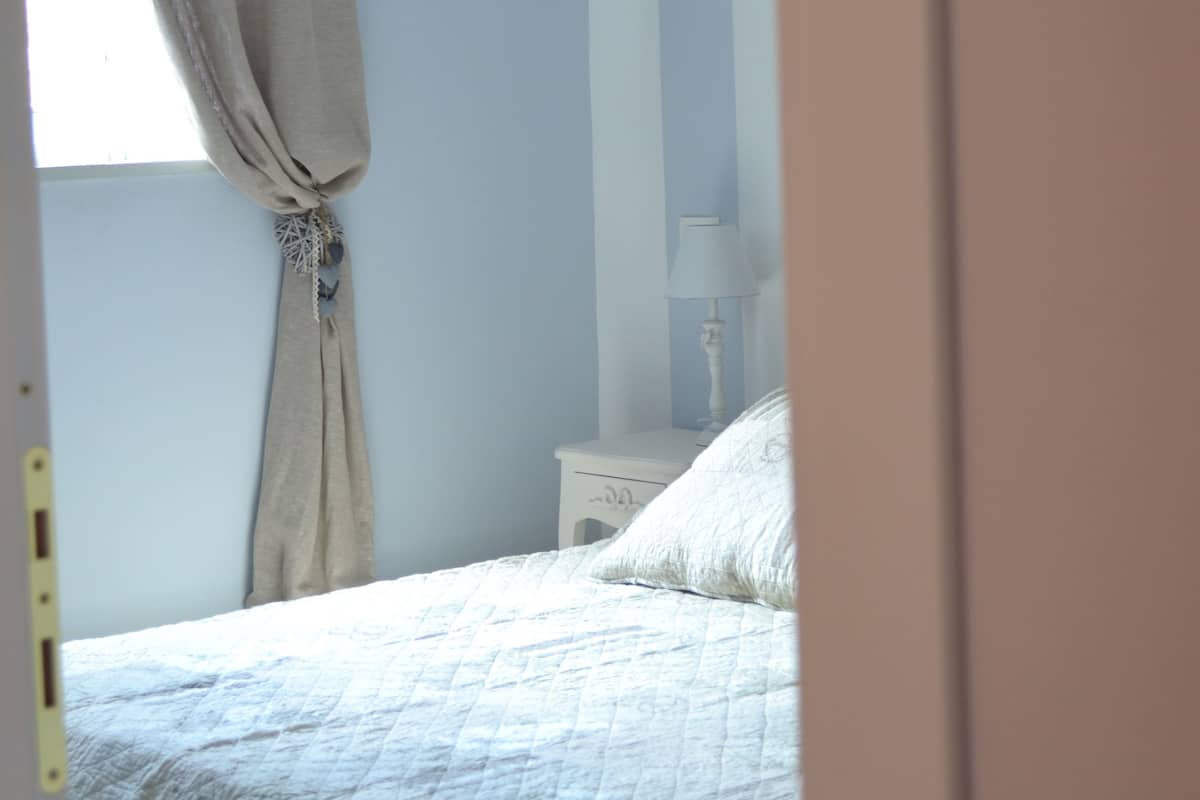 Een slaapkamer met een bed, nachtkastje, lamp en een raam met gordijnen.