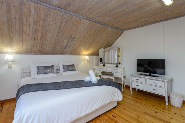 A bedroom with a wooden ceiling, a large bed, a TV, a dresser, and a mirror. - Zesty Guesthouse (Port Edward)