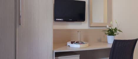 Habitación de hotel con un armario de madera, un escritorio con televisor de pantalla plana, una pequeña planta en maceta y una silla.