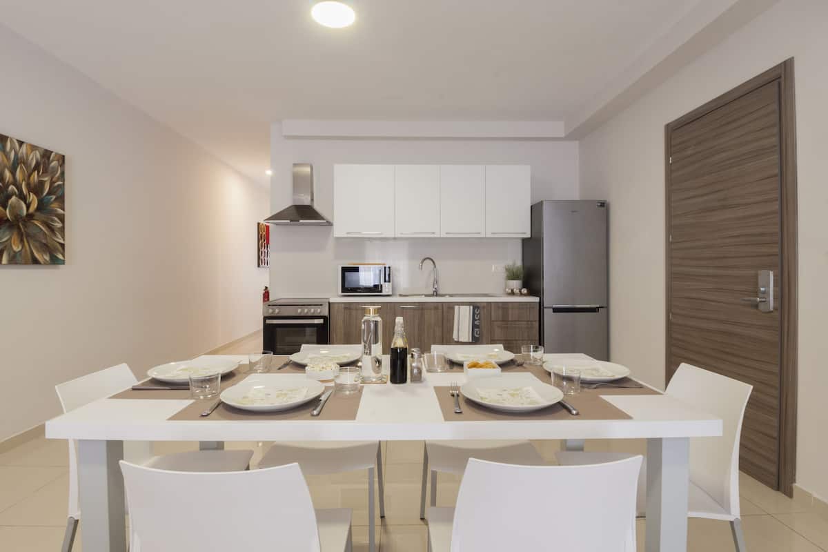 Une cuisine moderne avec des meubles blancs, un réfrigérateur en acier inoxydable et un coin repas comprenant des chaises et une table blanches, le tout disposé pour accueillir quatre personnes.