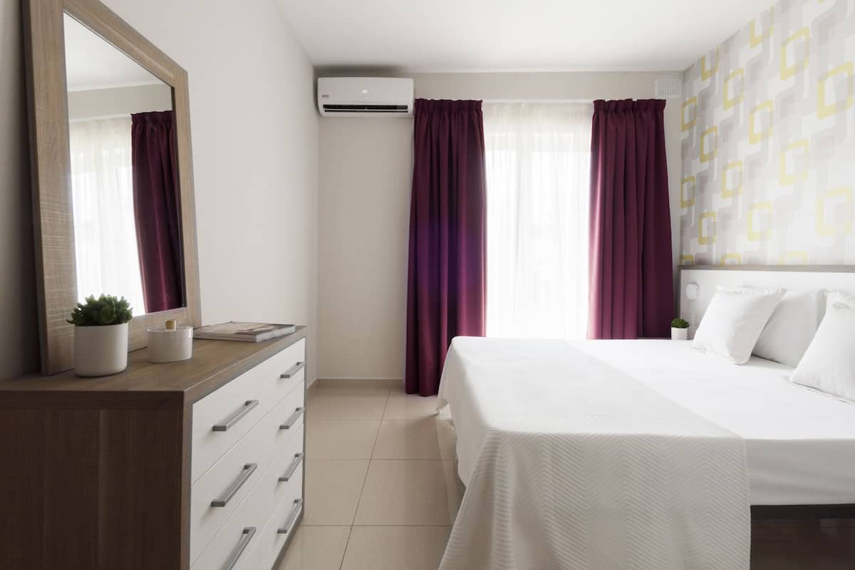 Une chambre d’hôtel avec un lit, une commode, un miroir, un climatiseur et des rideaux.