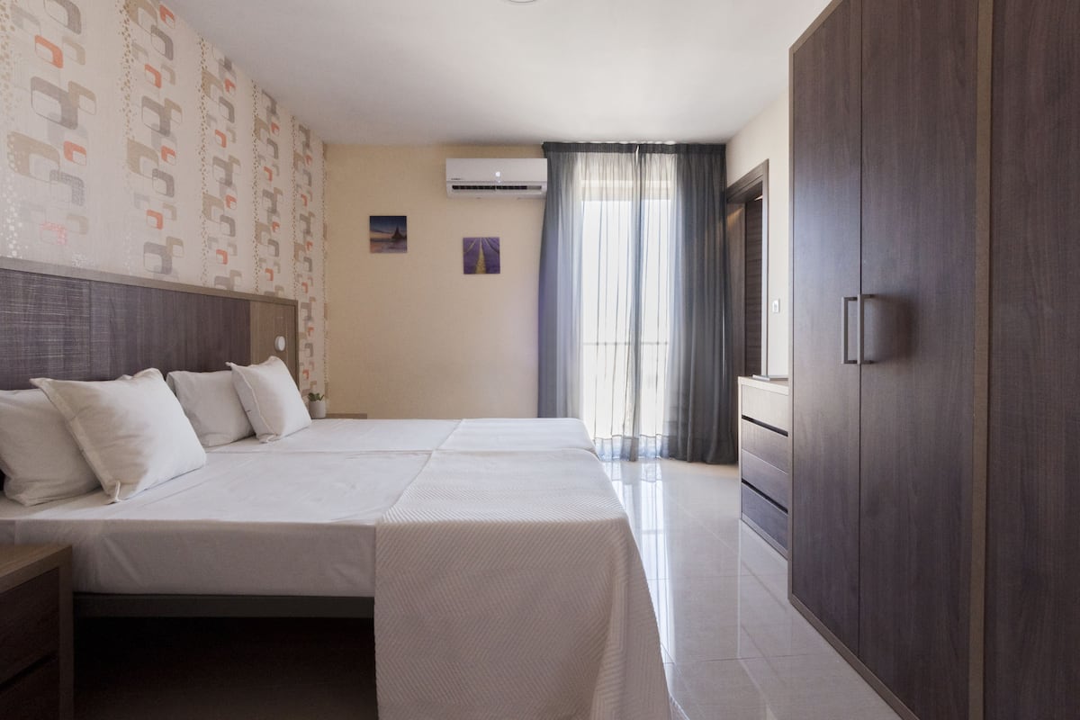 Une chambre d’hôtel avec un grand lit, une armoire, une table de chevet et une fenêtre avec des rideaux.