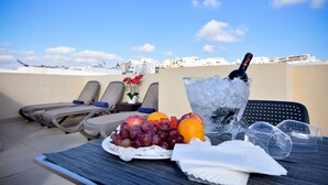 Een terras op het dak met lounge fauteuils, een tafel met fruit, een fles champagne en ijs.