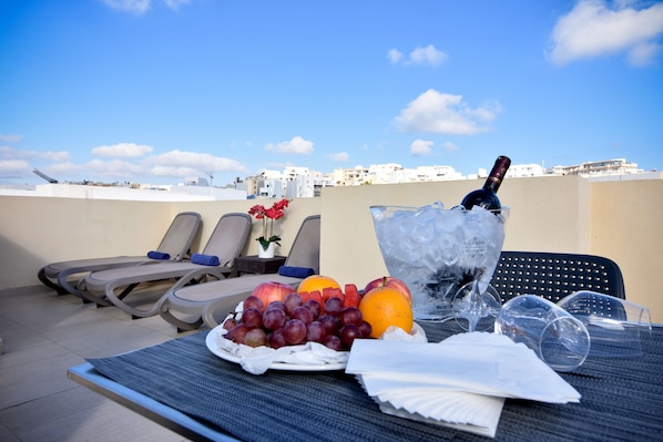 Una terraza en la azotea con sillones de descanso, una mesa con fruta, una botella de champán y hielo.