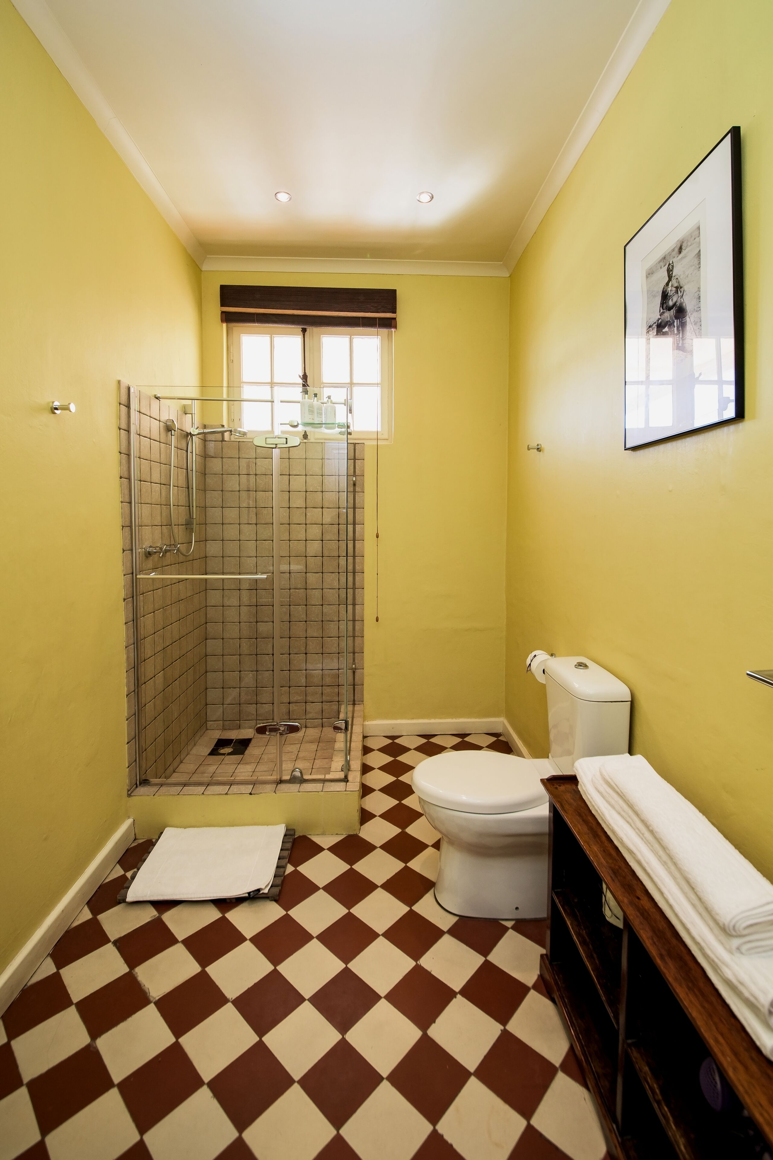 A bathroom with yellow walls, a checkered floor, a shower, a toilet, and a framed picture on the wall.