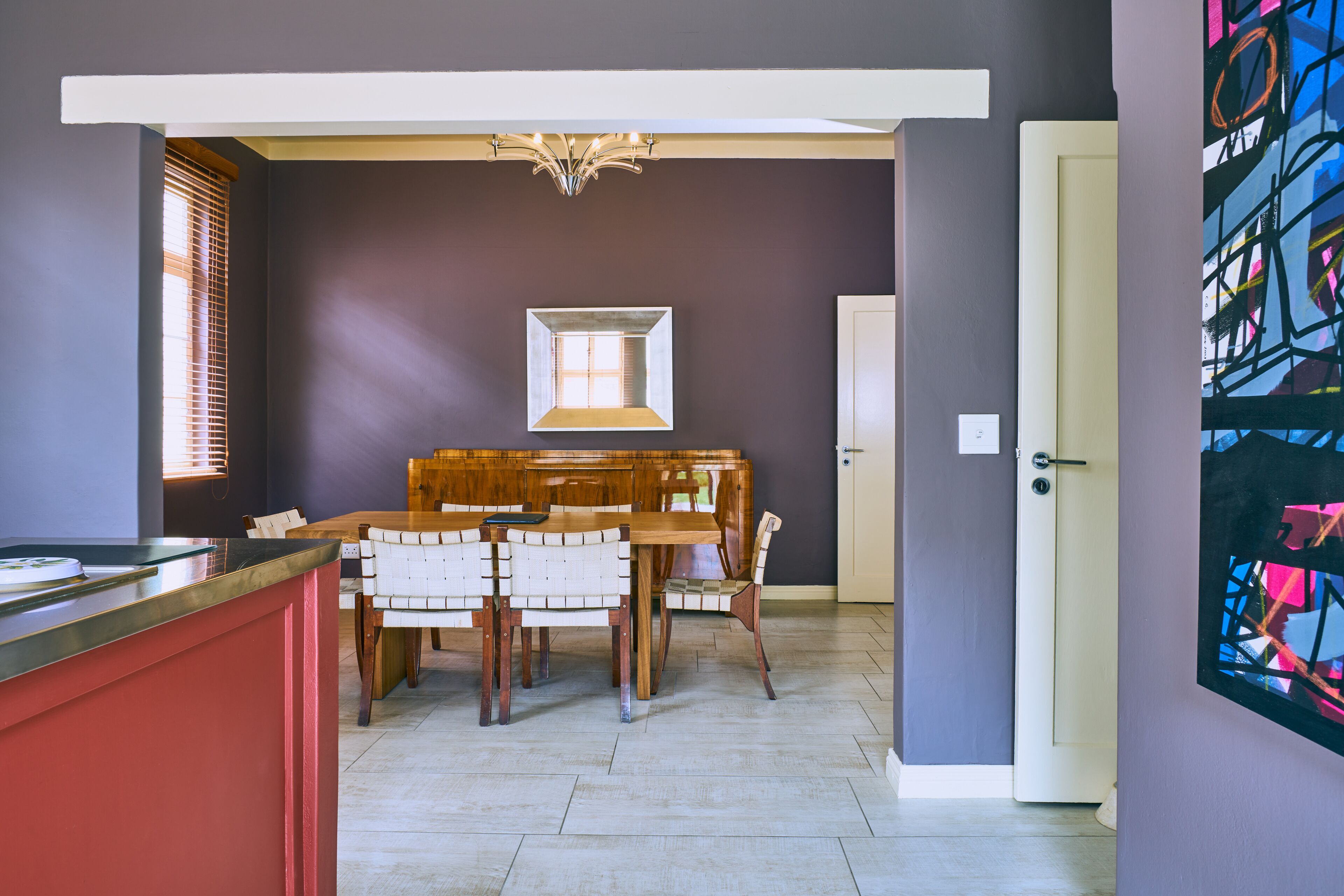 Un coin repas avec une table et des chaises en bois, un luminaire suspendu et un miroir encadré au mur.
