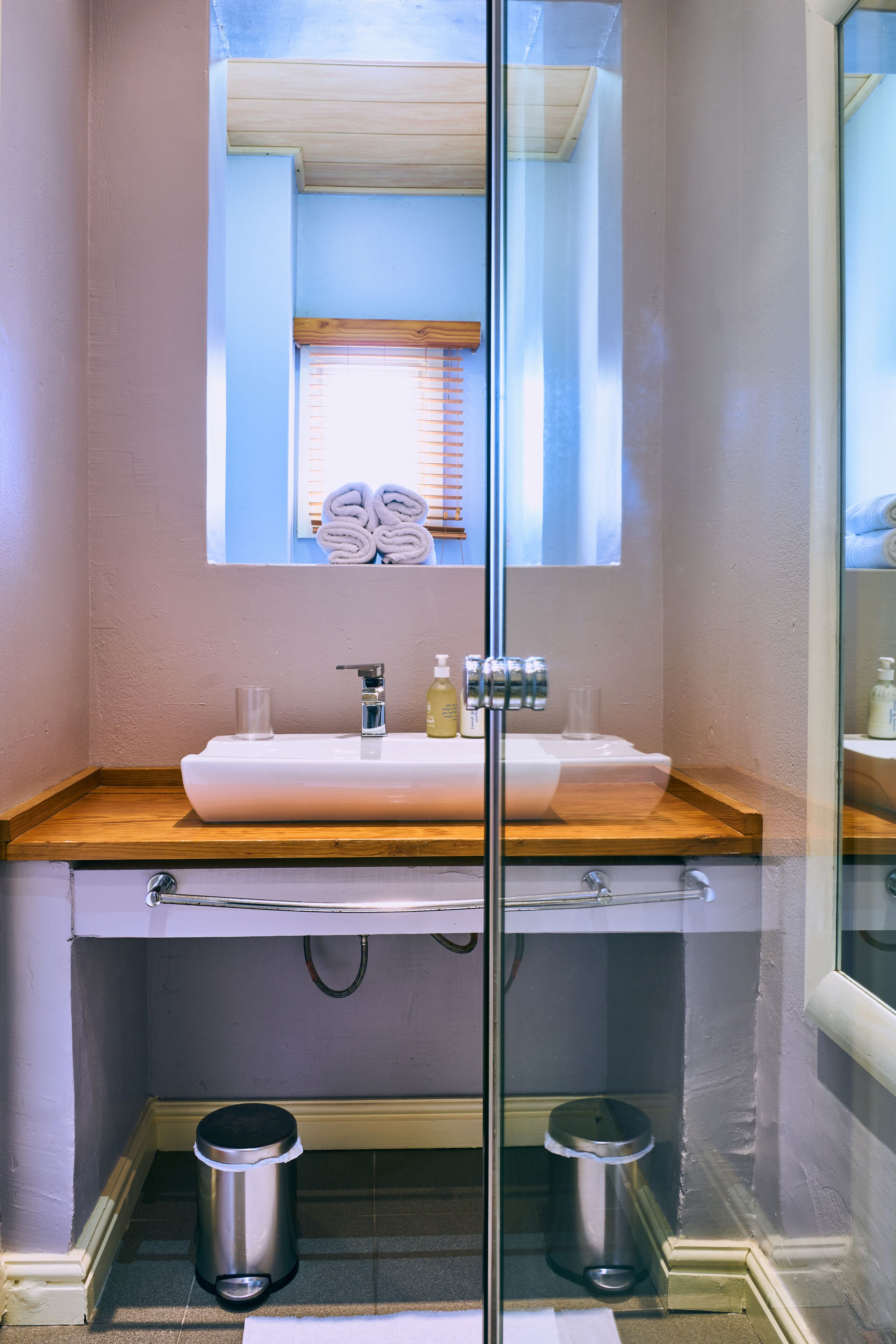 A bathroom with a glass shower enclosure, a wooden countertop sink, and two trash bins.