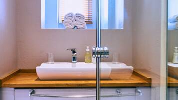 A bathroom with a glass shower enclosure, a wooden countertop sink, and two trash bins.