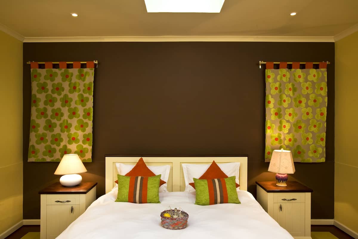 Habitación de hotel con una cama grande, dos mesitas de noche con lámparas y cortinas con estampado floral.