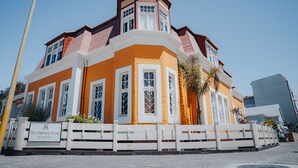 A corner building with a white fence, a sign reading "The Charming House," and a clear blue sky. - Villa Margherita (Swakopmund)