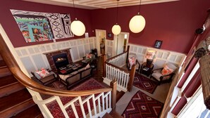 A staircase with a wooden handrail and white balusters, leading to a living area with a fireplace, a sofa, and patterned rugs. - Villa Margherita (Swakopmund)