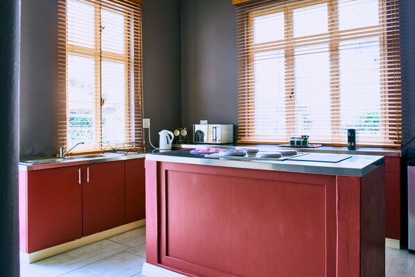 A kitchen with a red island, wooden blinds, and modern appliances.