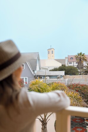 A person in a hat overlooking a residential area with a church tower, palm trees, and a patterned patio.