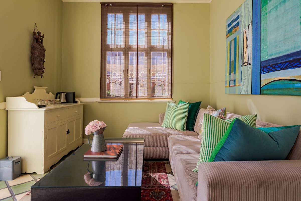 Una sala de estar con un sofá, una mesa de centro, un mueble, una ventana con persianas y un cuadro en la pared.