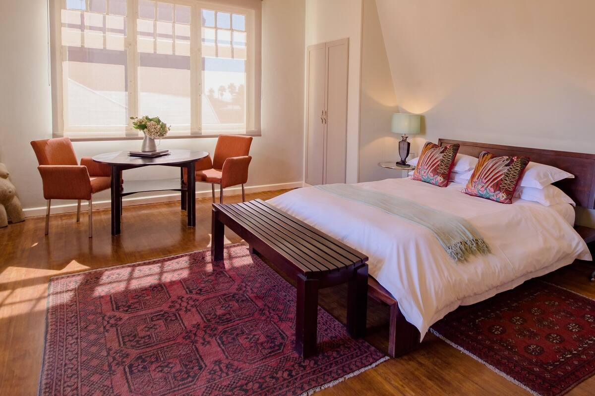 Un dormitorio con una cama grande, un escritorio con dos sillas, un banco y una ventana con vistas.