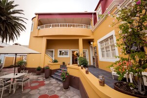 Un edificio amarillo con balcón, plantas en macetas y mesas al aire libre.