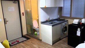 Cocina compacta con lavadora, lavamanos y un inodoro visible a través de un panel de vidrio.