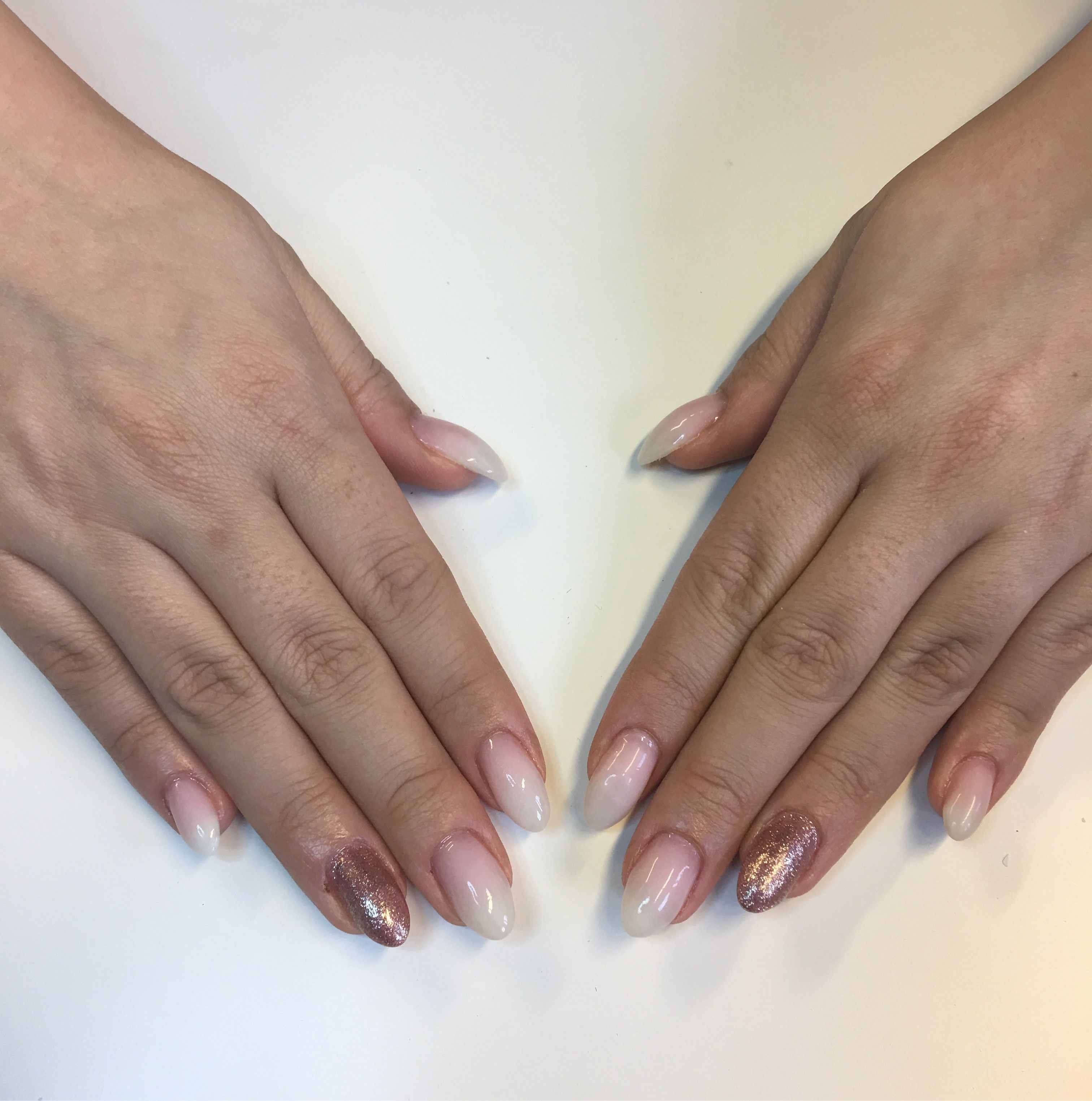 A pair of hands with manicured nails, one with a clear polish and the other with a glittery design.