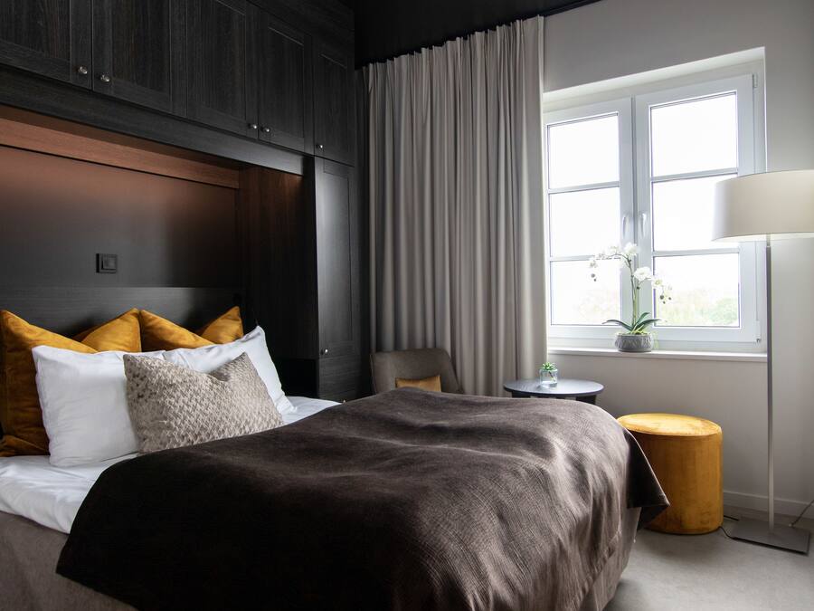 A hotel room with a bed, a nightstand, a lamp, a window with curtains, and a view of the outdoors.
