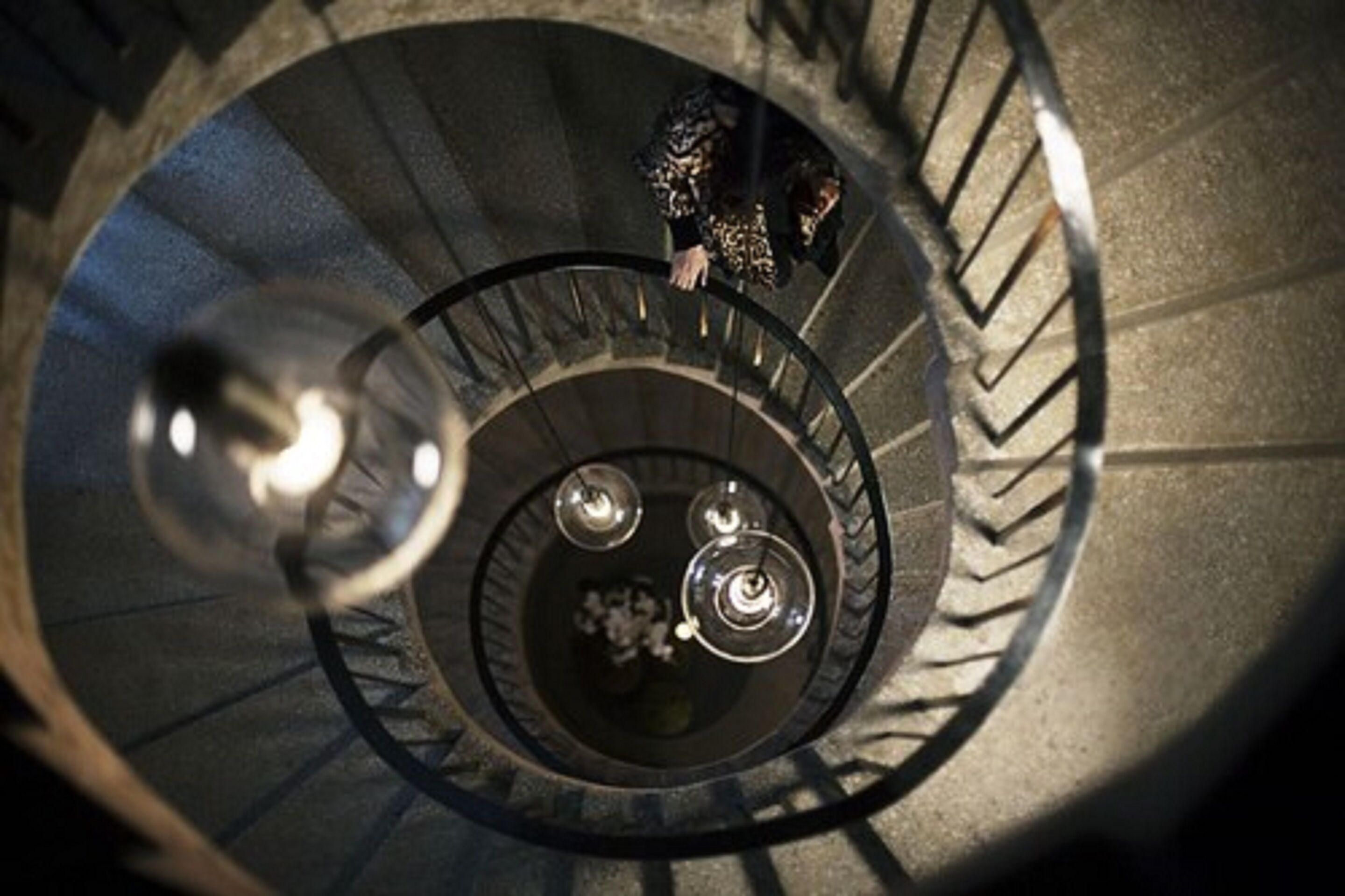 Una escalera de caracol con barandilla y una persona bajando.