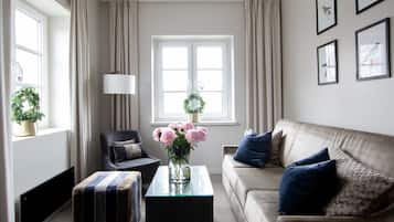 A living room with a sofa, armchair, ottoman, and a glass coffee table with a vase of flowers.