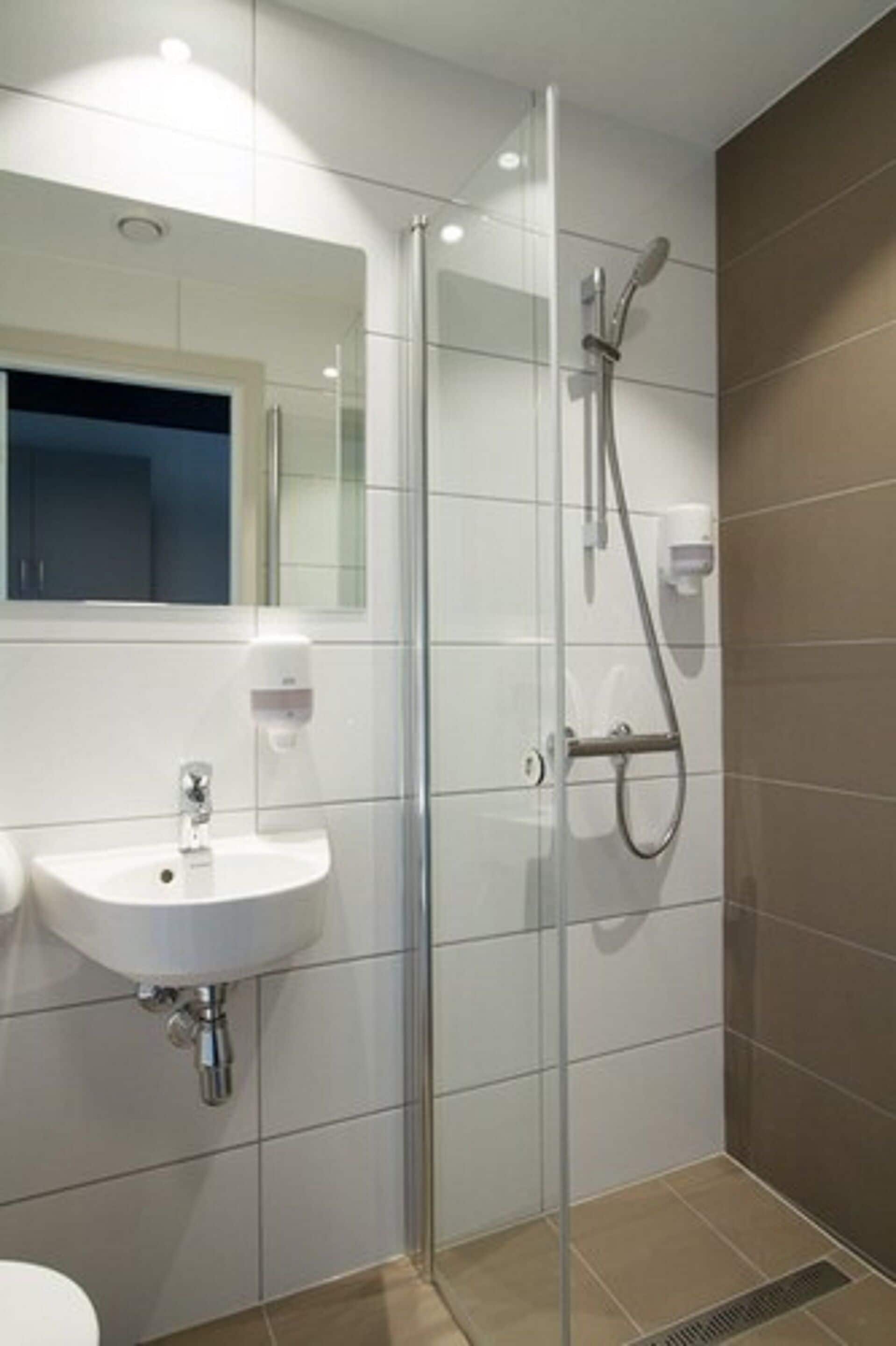 Een moderne badkamer met een douchecabine van glas, een witte wastafel en een spiegel erboven.