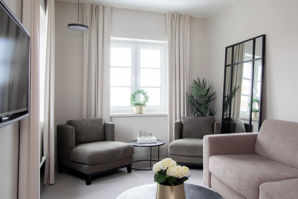 Ein modernes Wohnzimmer mit zwei Sofas, einem Couchtisch, einem Fernseher und einem großen Fenster mit Vorhängen.