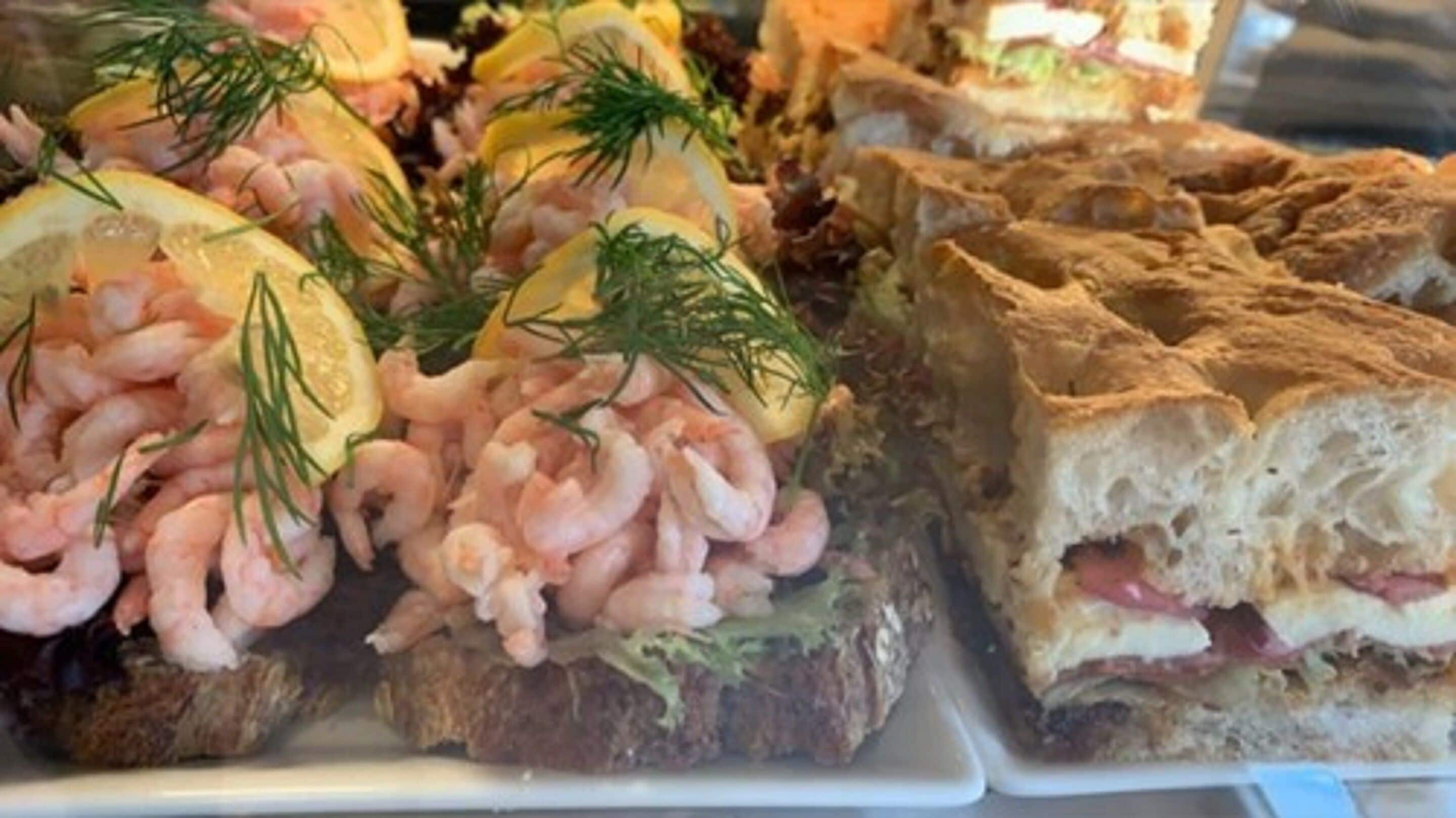 Variedad de alimentos, incluyendo camarones y sándwiches, probablemente parte de un bufé o servicio de catering.