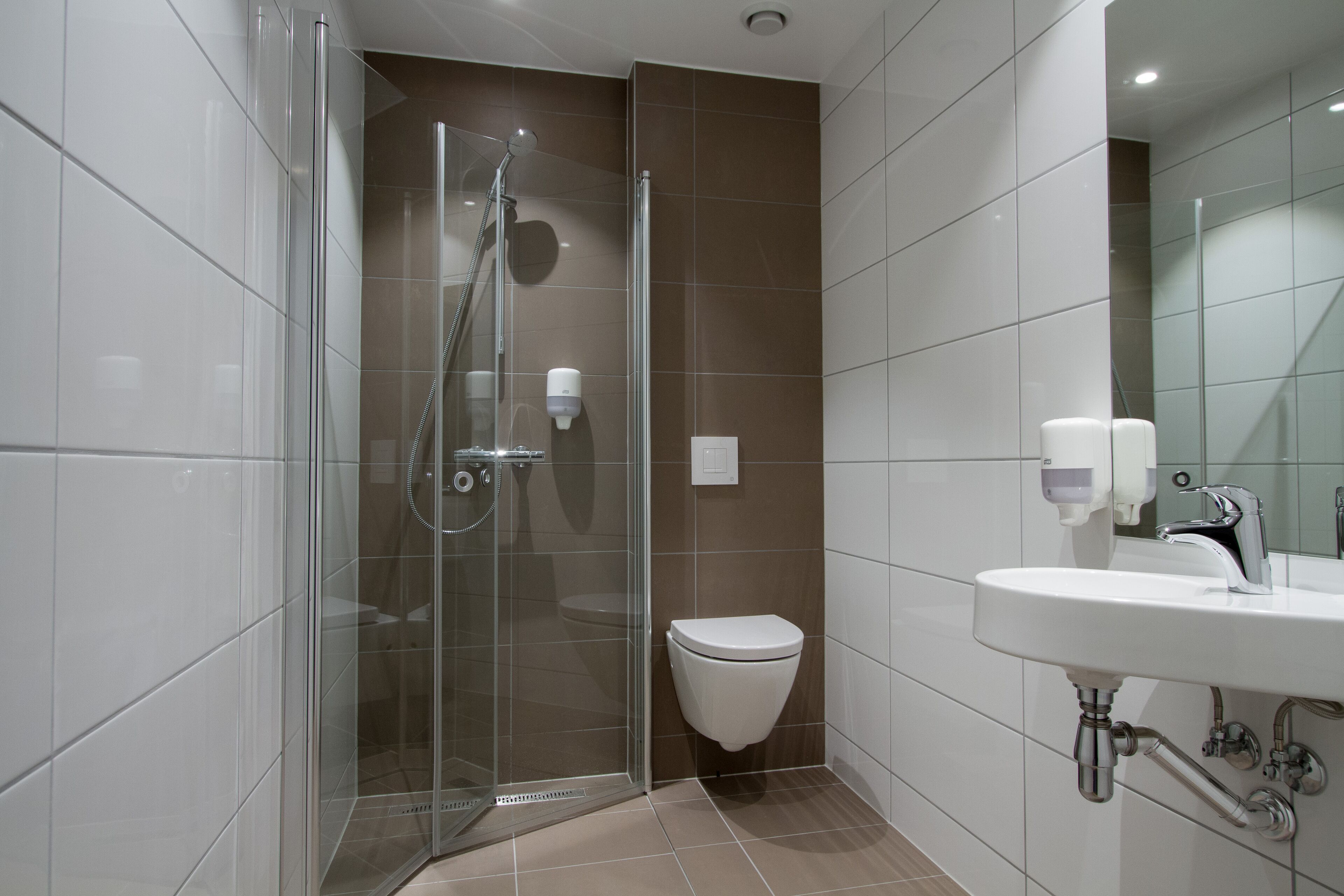 Une salle de bain moderne avec une douche à parois de verre, des toilettes blanches et un lavabo avec un miroir.