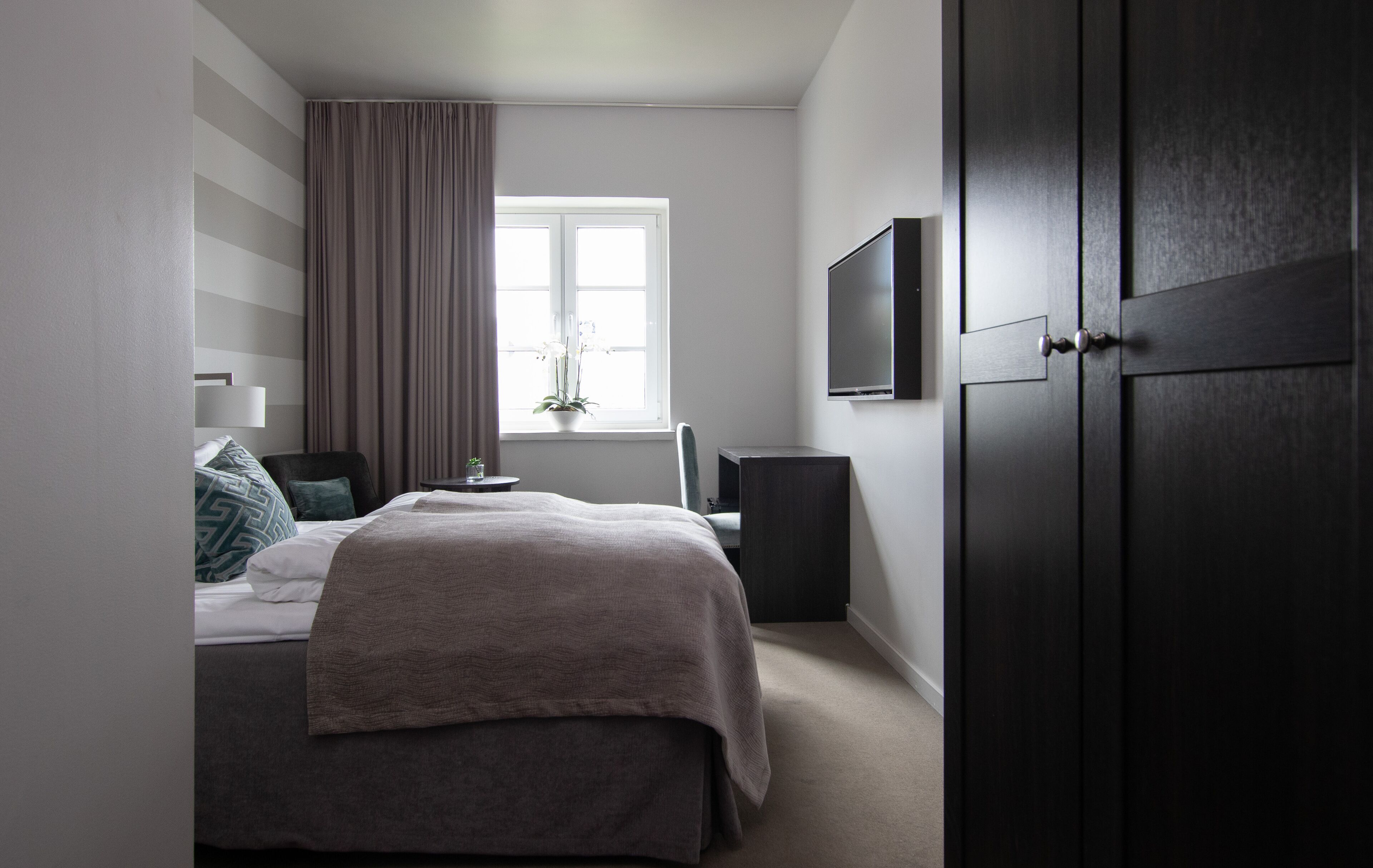 Een moderne slaapkamer met een bed, nachtkastje, lamp en een raam met gordijnen.