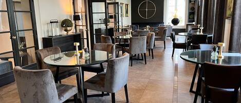 A modern dining area with round tables and velvet chairs, a black wall with a clock, and artwork on the walls.