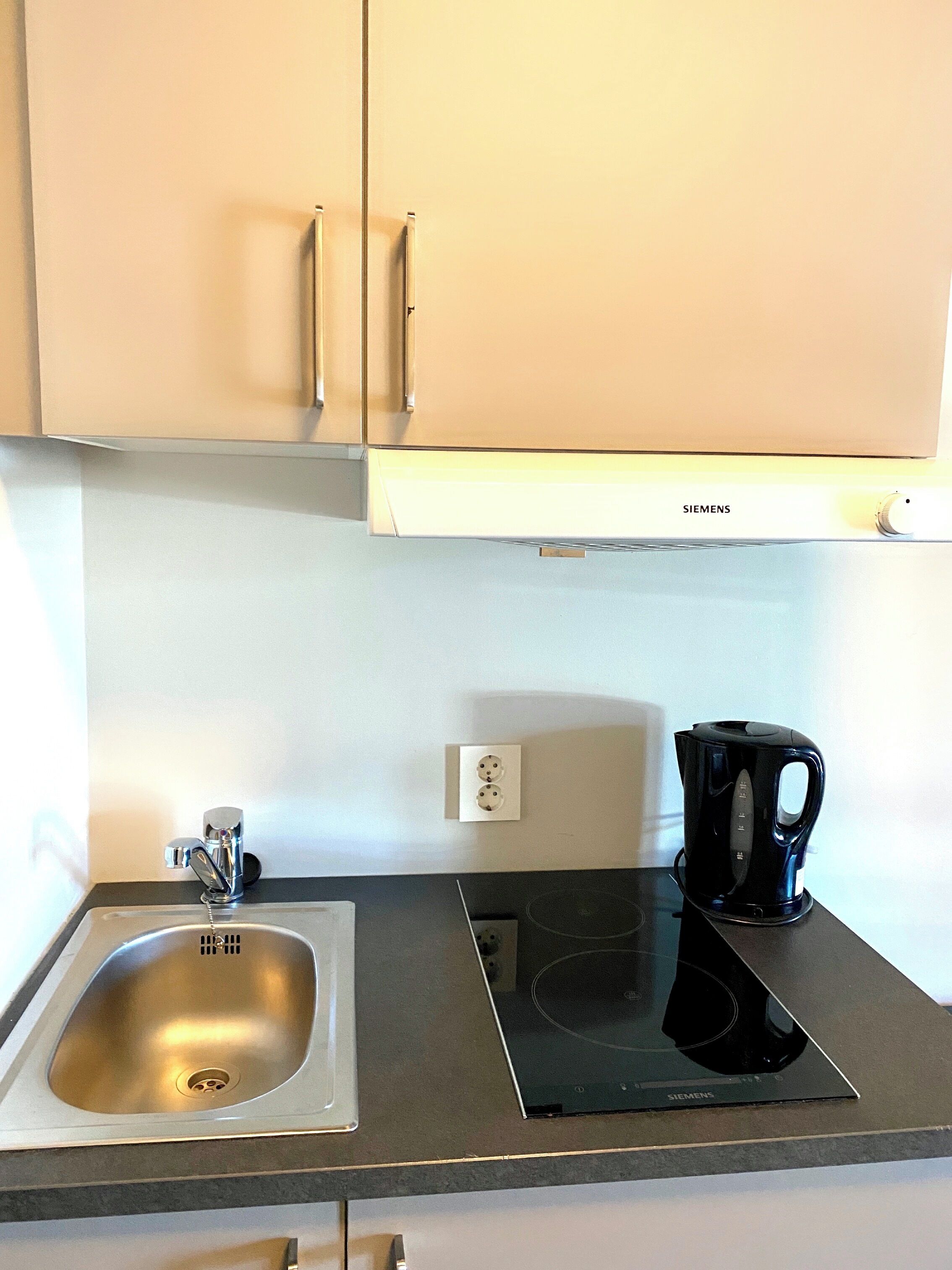 Una cocina con un lavamanos de acero inoxidable, una tetera eléctrica negra y una placa de inducción Siemens.