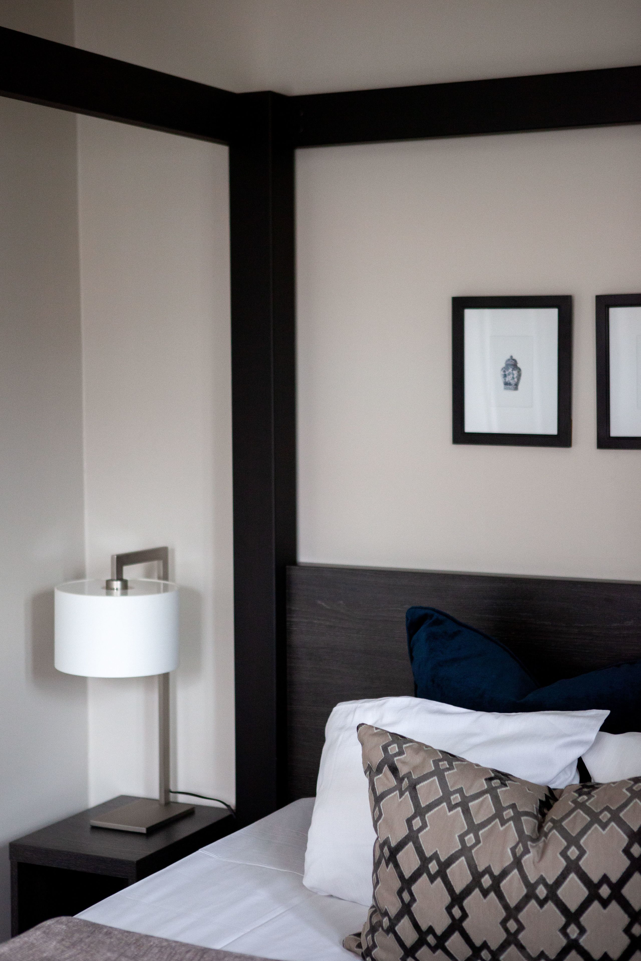 Habitación de hotel con cama, mesita de noche con lámpara y dos cuadros en la pared.