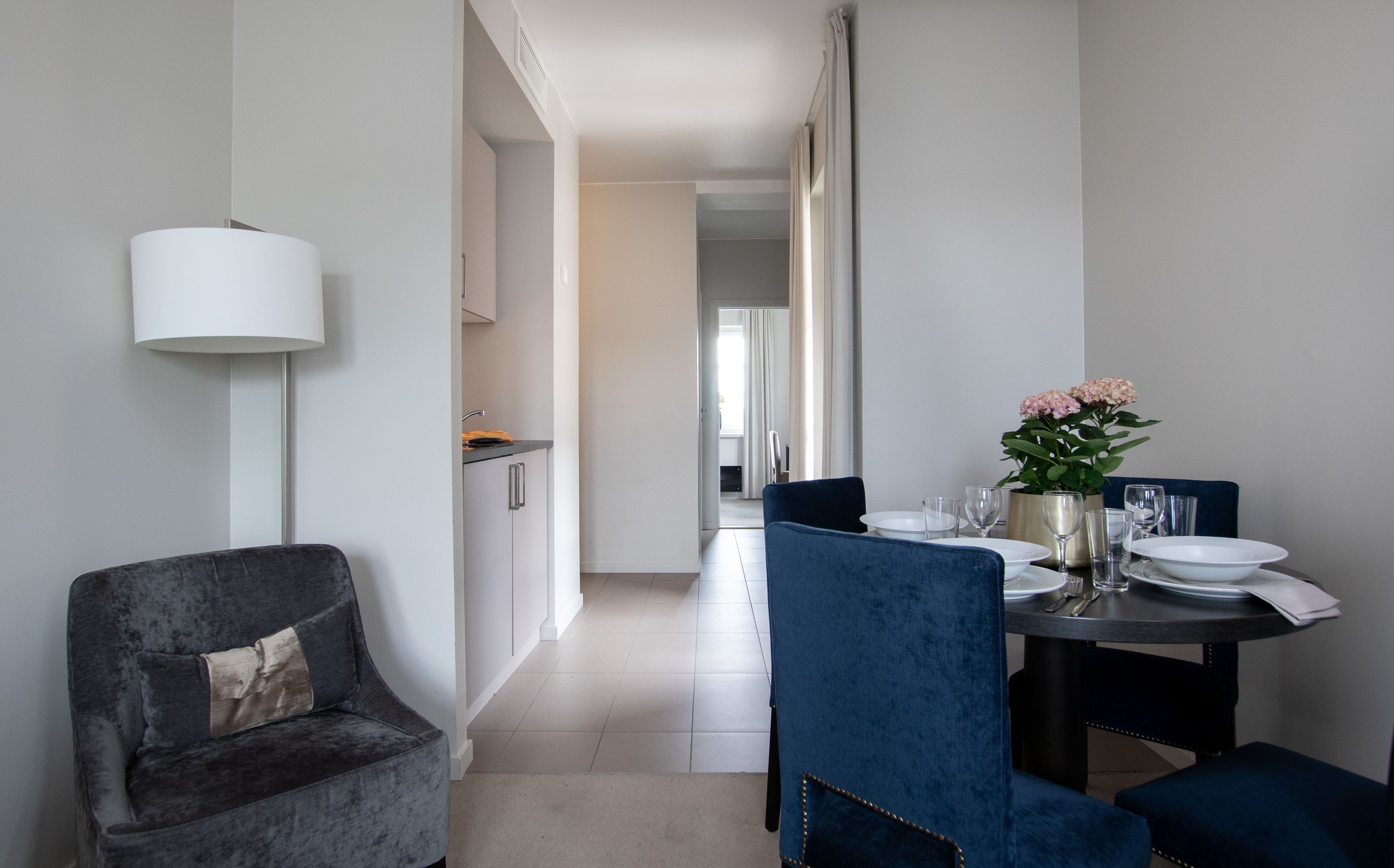 Un espace repas moderne avec une chaise à l’assise rembourrée de couleur bleu foncé, une table dressée avec des assiettes, des verres et une plante en pot.