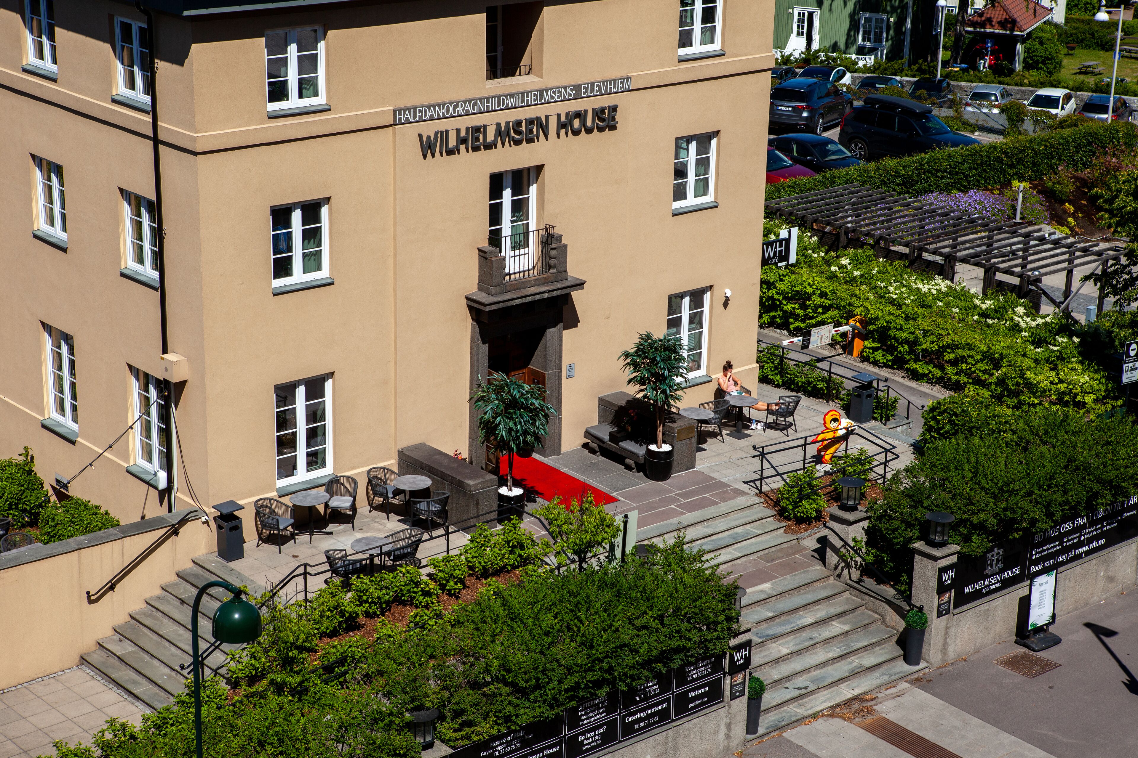 Un edificio con un cartel que dice "Wilhelmsen House". Hay zonas de estar al aire libre con mesas y sillas.