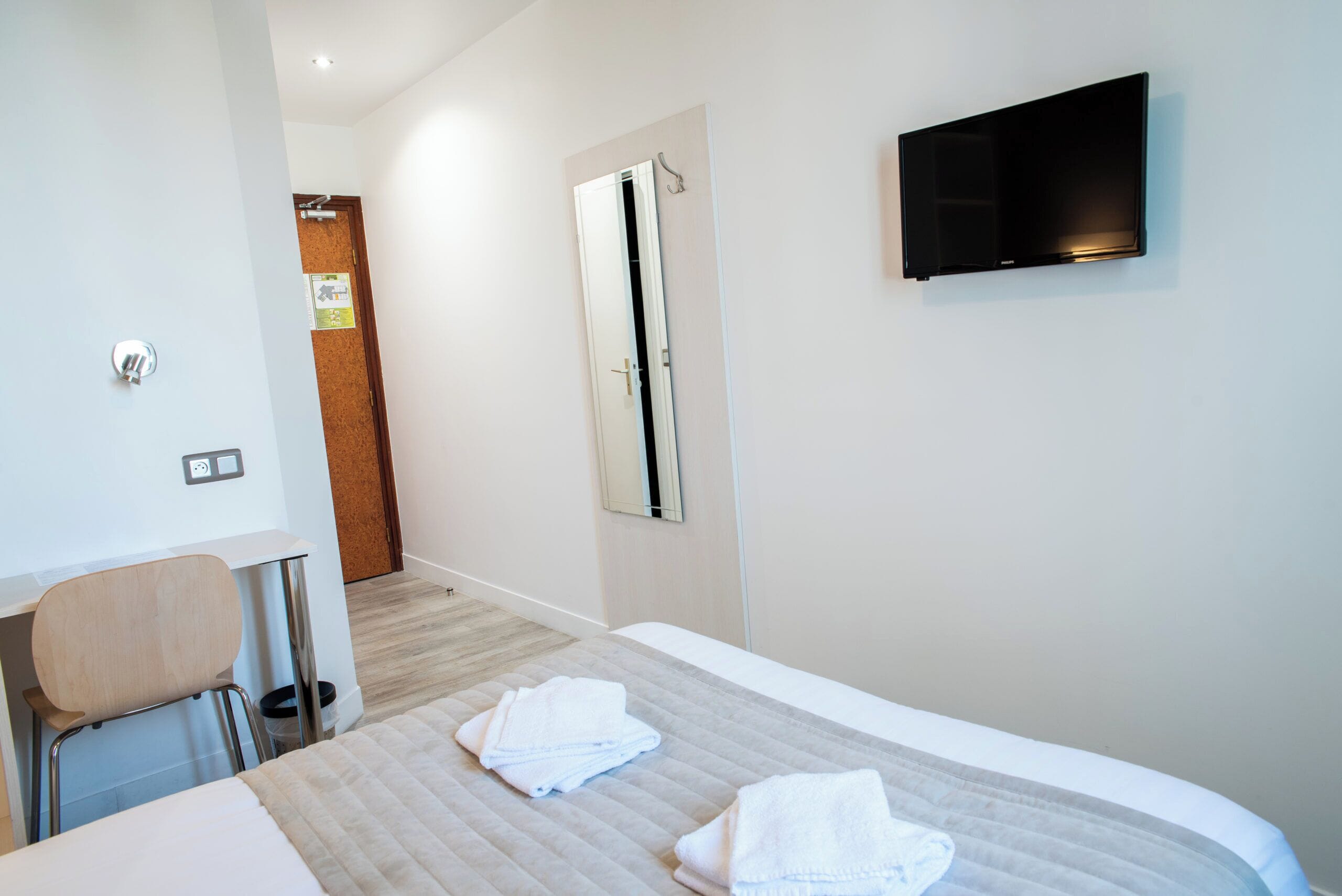Habitación de hotel con cama, televisión montada en la pared, escritorio y silla.
