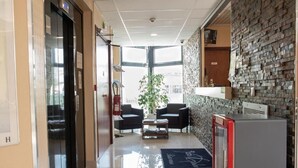 Un hall d’hôtel comprenant un comptoir d’accueil, un espace salon et une grande fenêtre laissant entrer la lumière naturelle.