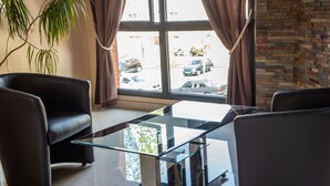 Une pièce moderne avec une table basse en verre, des fauteuils en cuir, une grande fenêtre avec des rideaux et une vue sur les voitures garées à l’extérieur.