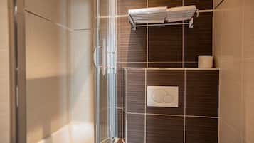 Un baño moderno con cabina de ducha de vidrio, inodoro empotrado y un perchero para toallas.
