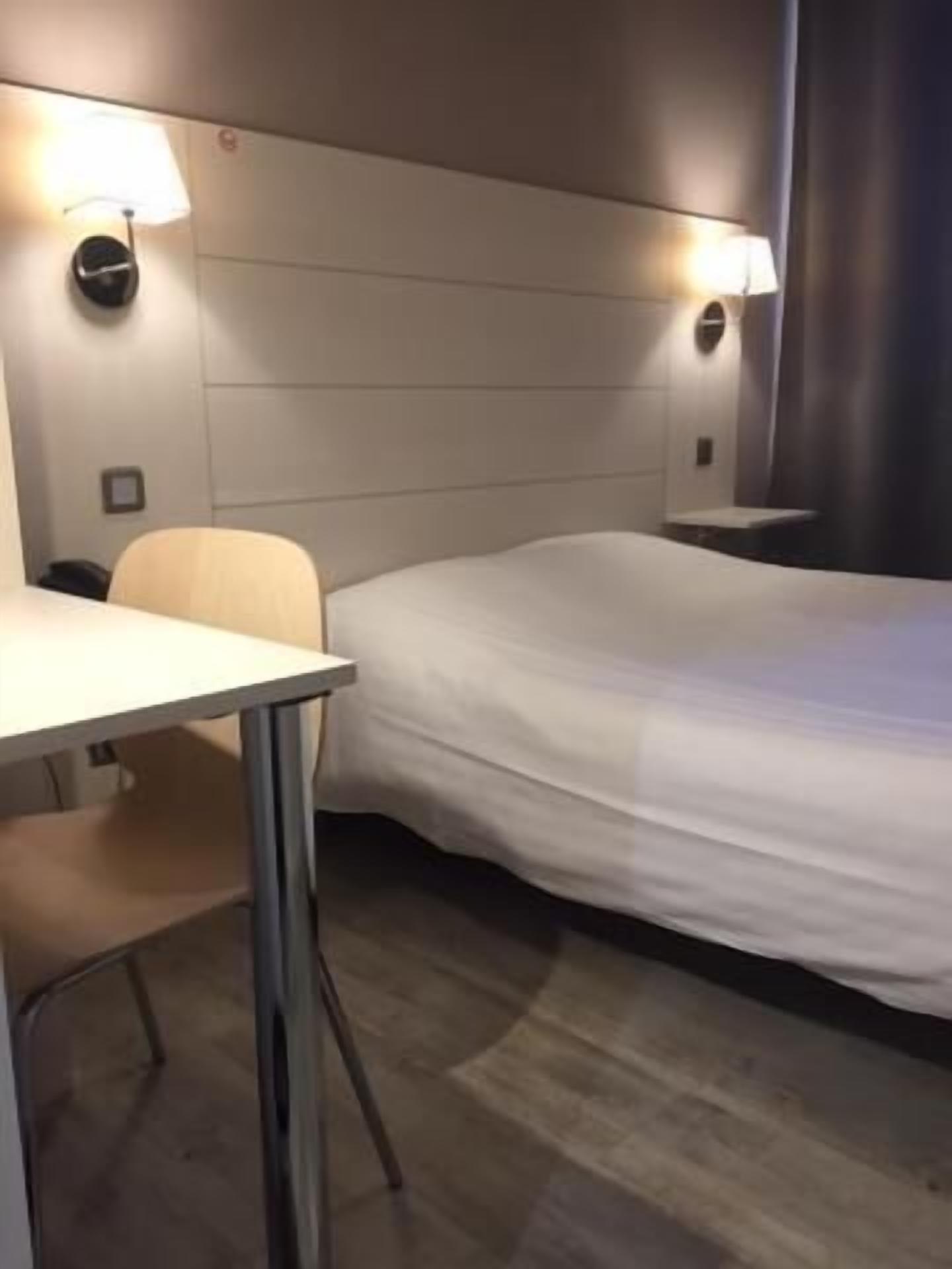 A hotel room with a bed, a desk, and two wall-mounted lamps.