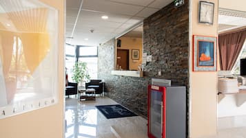 Un vestíbulo de hotel con una pared de ladrillo, un refrigerador rojo, un reloj y un cuadro en la pared.
