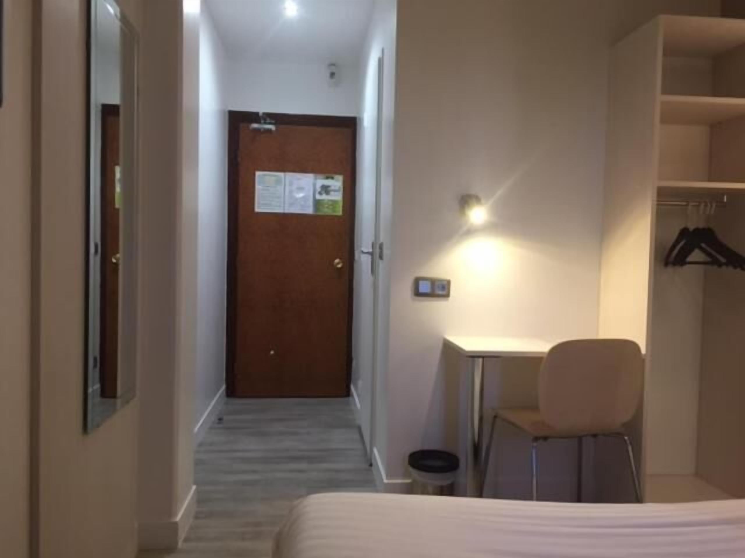 A hotel room with a bed, a desk, a chair, and a wardrobe.