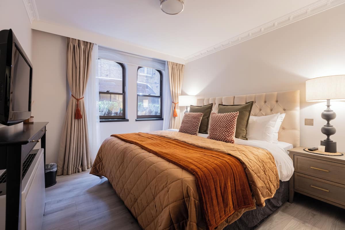A hotel room with a bed, bedside table, lamp, and a window with curtains.