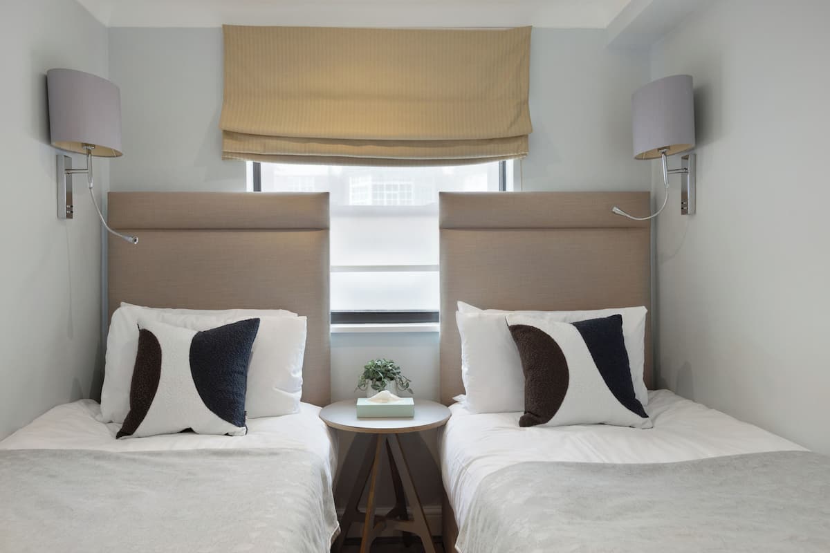A hotel room with two beds, a small table with a plant, and two wall-mounted lamps.