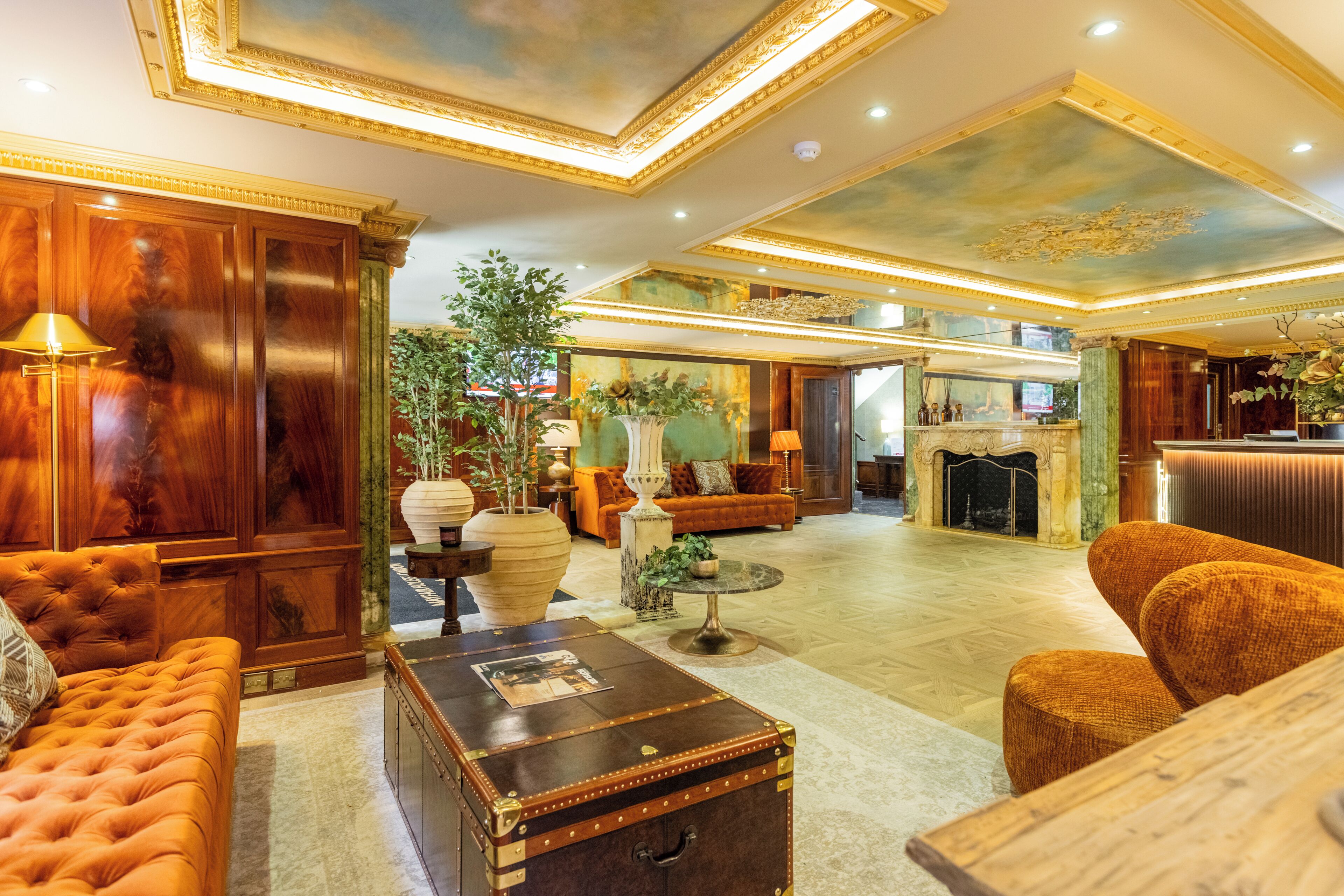 A spacious lobby with a grand staircase, a fireplace, and a large potted plant.
