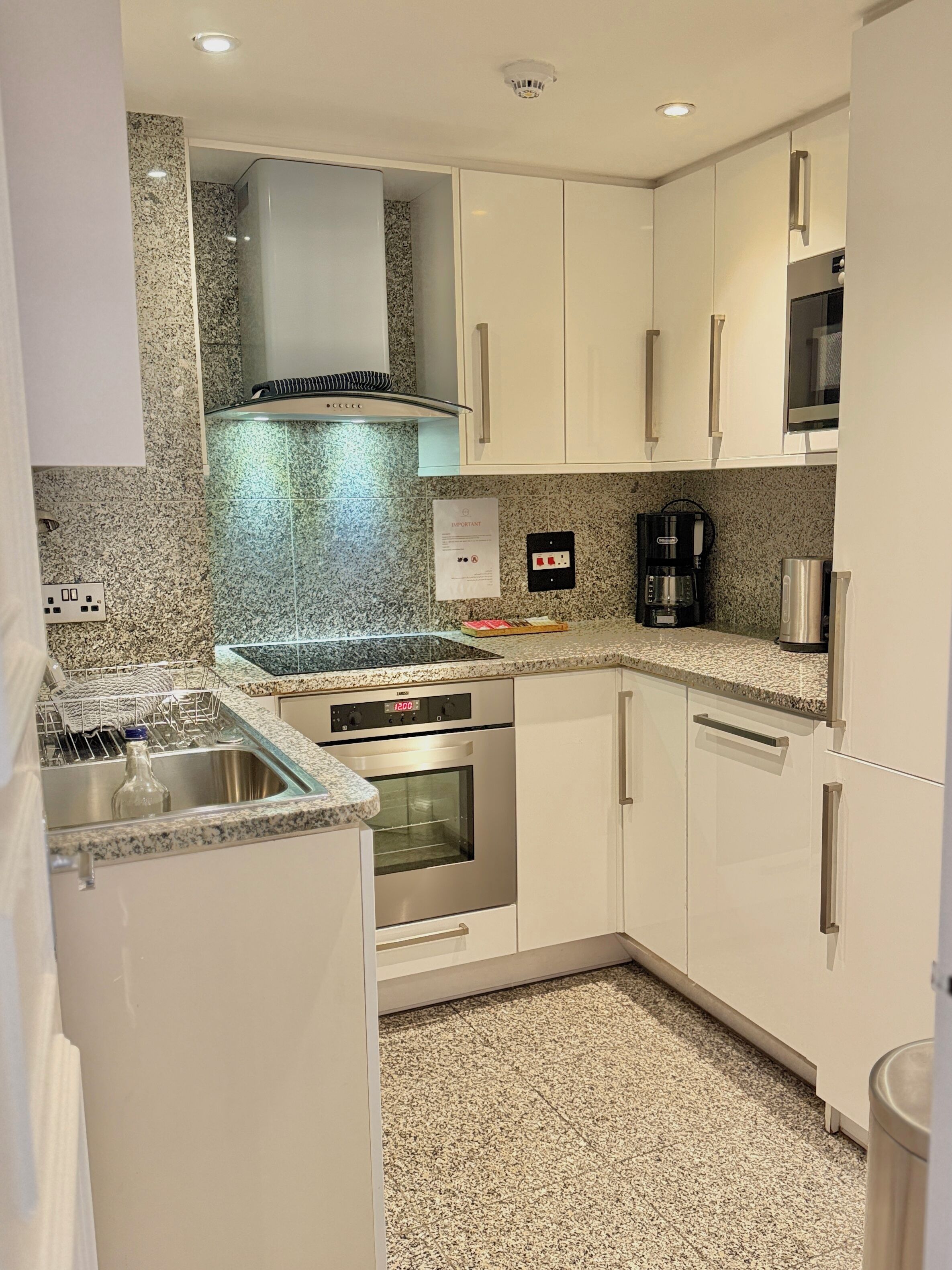A compact kitchen with white cabinets, a stainless steel sink, a built-in oven, and a coffee maker.