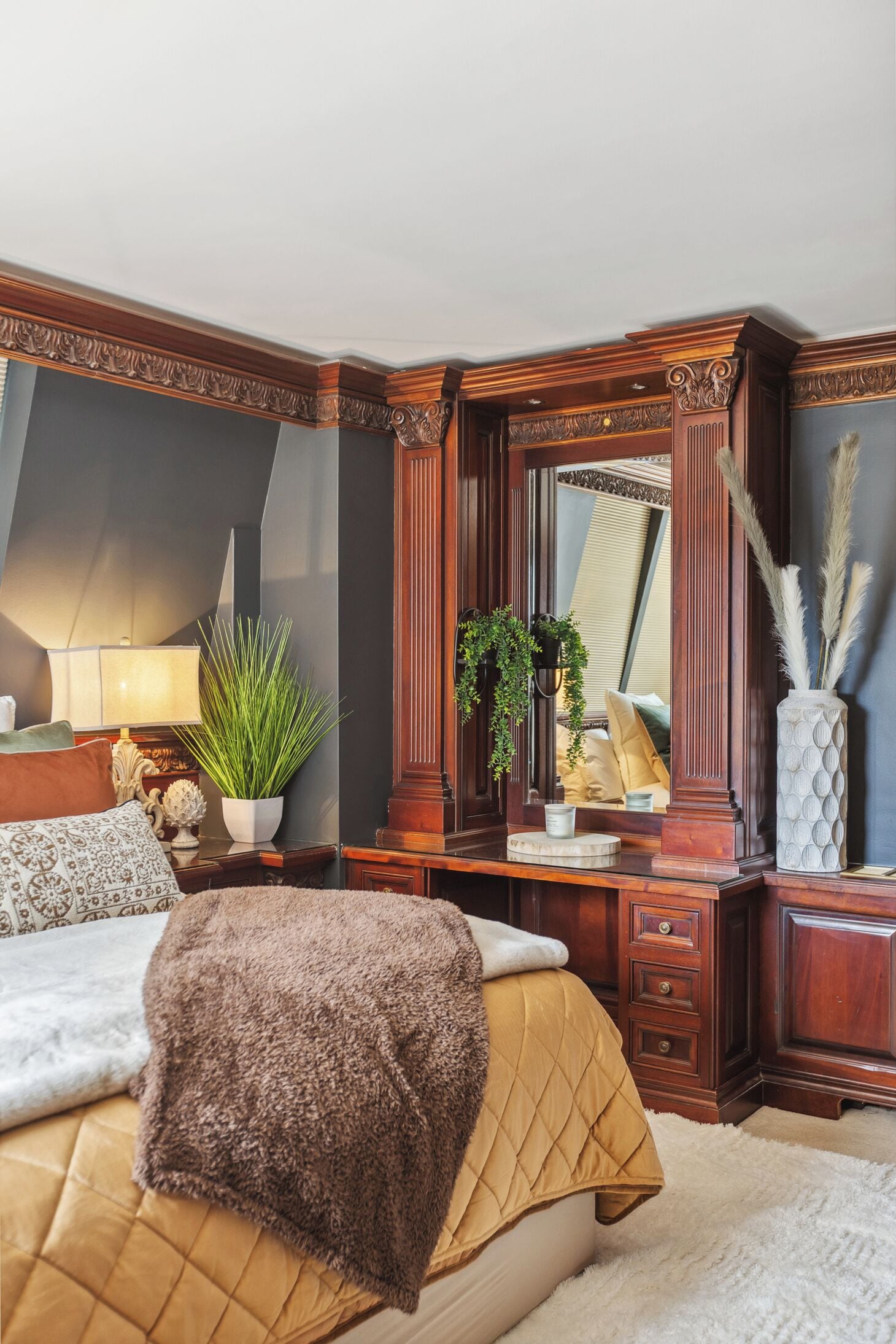 A bedroom with a large bed, a dresser, a mirror, and a potted plant.