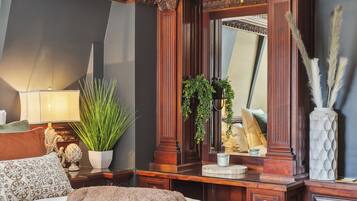A bedroom with a large bed, a dresser, a mirror, and a potted plant.